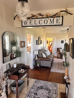 Ein Wohnzimmer mit einem 'WELCOME'-Schild, einem Spiegel, einem Sofa, einem Couchtisch und einem Teppich.