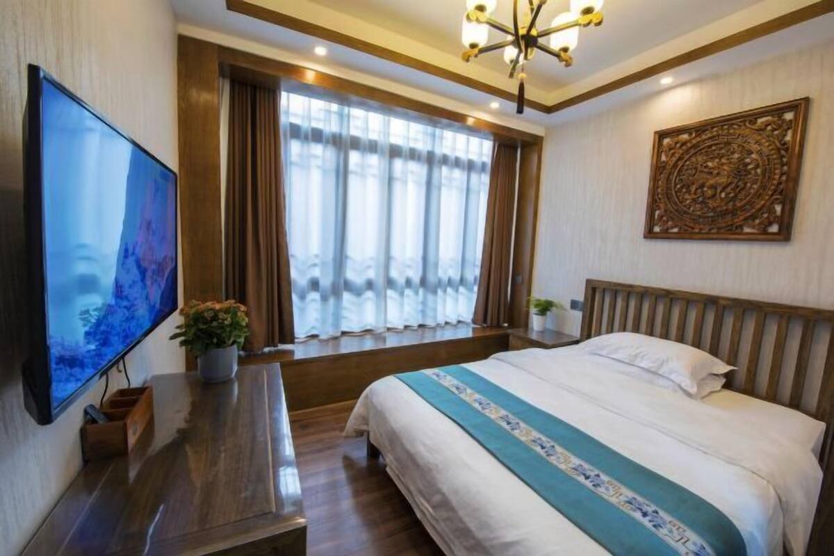 Quarto com cama, televisão, janela com cortinas, cabeceira de madeira e um detalhe decorativo na parede.