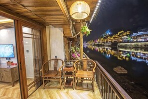 Una terraza de madera con sillas, una mesa, un televisor y vistas de un río de noche.