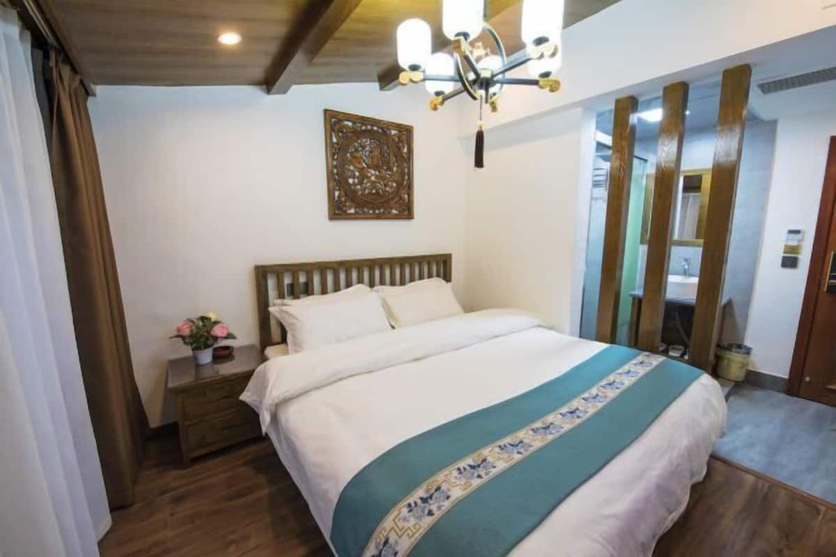 Quarto com cama, mesa de cabeceira com um vaso de flores, lustre e um objeto decorativo na parede.