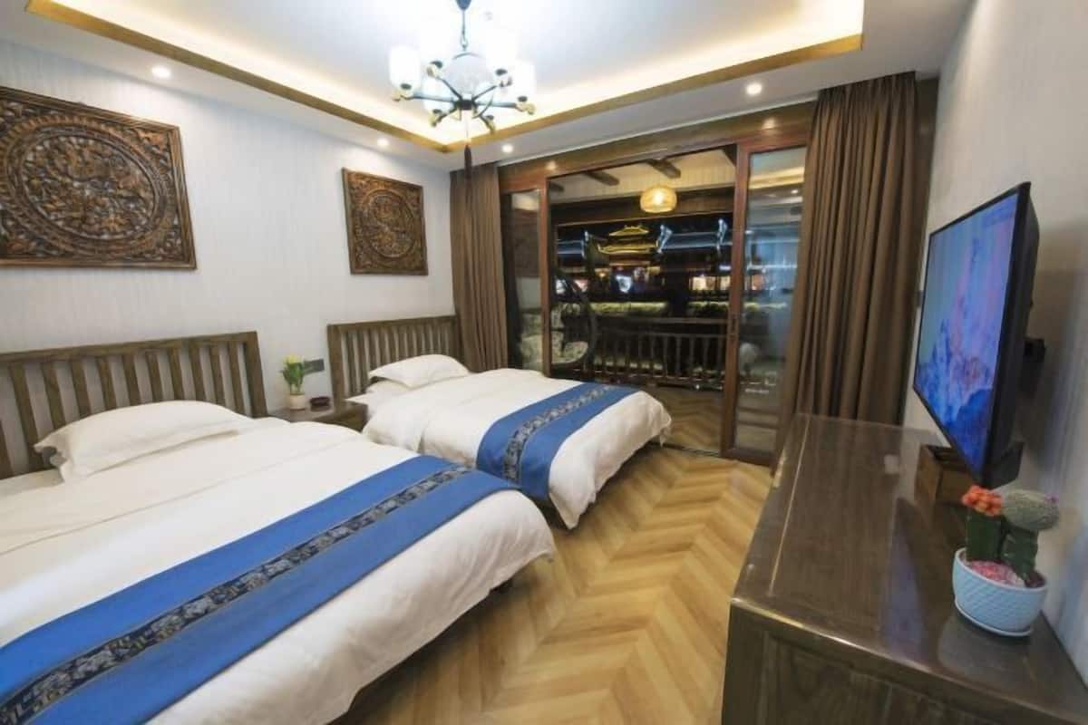 Quarto de hotel com duas camas, uma TV, uma escrivaninha e vista para um restaurante através de uma porta de vidro.