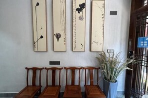 A wall with four vertical paintings, a row of wooden chairs, and a potted plant. - Phoenix Tuojianglou Diaojiaolou Inn (Fenghuang County)