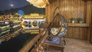 Una terraza de madera con una silla colgante, una mesa y vistas a edificios tradicionales al otro lado del agua.
