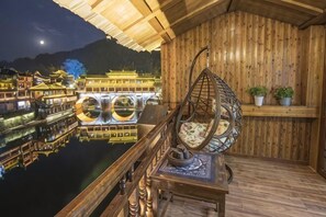 Una terraza de madera con una silla colgante, una mesa y vistas a edificios tradicionales al otro lado del agua.
