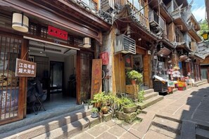A traditional building with a wooden facade, a signboard, and a small outdoor seating area with plants. - Phoenix Tuojianglou Diaojiaolou Inn (Fenghuang County)
