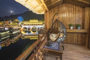 Enjoy breathtaking views of a traditional water village from this balcony, featuring a hanging chair and a small table.