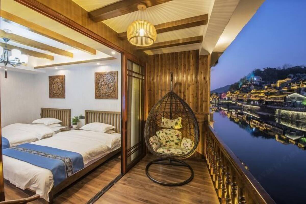 Quarto de hotel com uma cama, uma cadeira suspensa e vista para um corpo de água com edifícios.