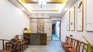 Zona de recepción con mostrador de madera, área de asientos con sillas de madera y un pasillo que conduce a otra habitación.