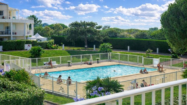 Una piscina rectangular rodeada por una valla blanca, con gente nadando y descansando alrededor.