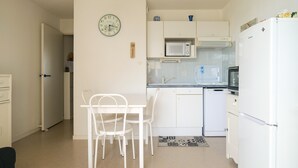 Una cocina compacta con electrodomésticos blancos, una mesa de comedor con sillas y un reloj en la pared.