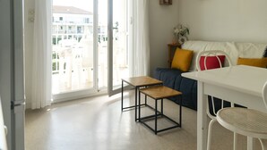 Una sala de estar moderna con un sofá, una mesita y una silla. Hay un ventanal corredero que da a un balcón al aire libre.