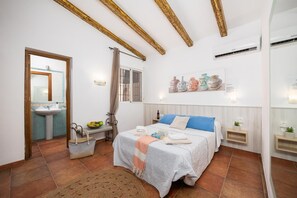 Une chambre à coucher comprenant un lit, des tables de chevet, un miroir, une fenêtre et un climatiseur fixé au mur.