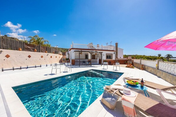 Une piscine avec des chaises longues, un patio couvert et un bâtiment doté d’un balcon.