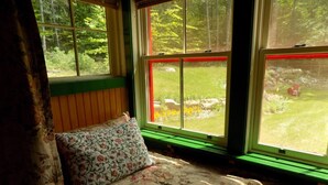 Una cama con ropa de cama floral, un banco verde y una ventana con vista a un jardín.