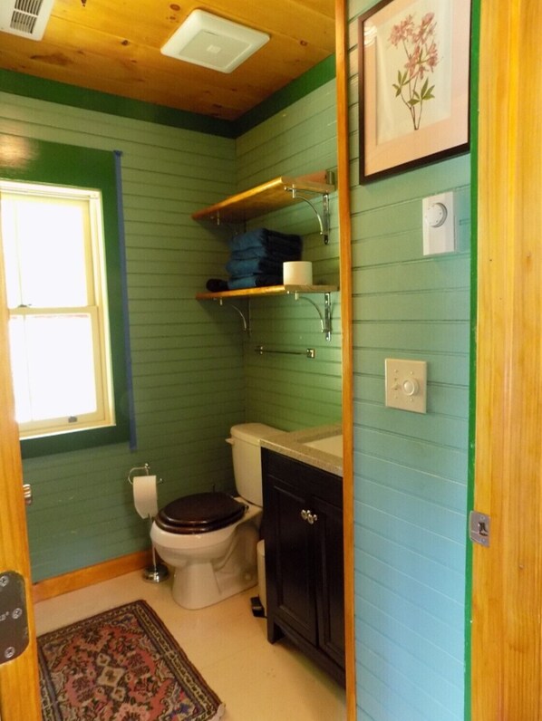 A small, compact bathroom with a toilet, sink, and shelves above the toilet.