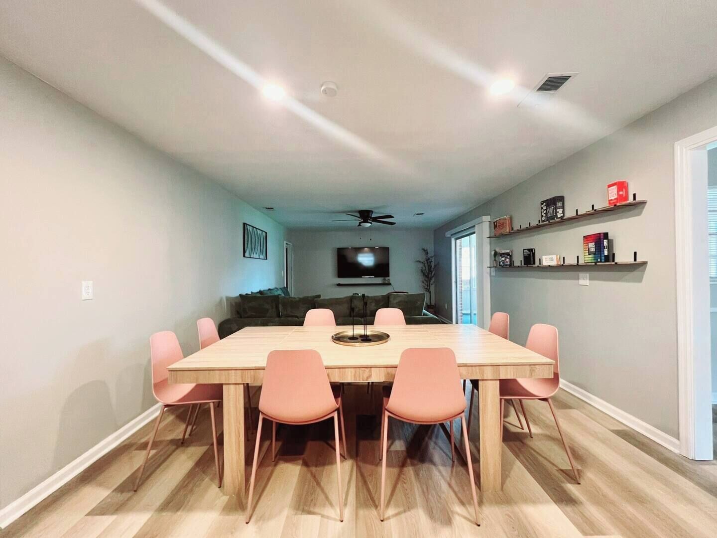 A dining area with a wooden table and pink chairs, a ceiling fan, and a TV in the background.