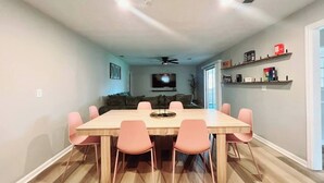 Een eetruimte met een houten tafel en roze stoelen, een plafondventilator en een televisie op de achtergrond.