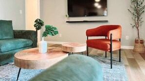 Een woonkamer met een groene bank, een rode stoel, een salontafel en een aan de muur bevestigde televisie.