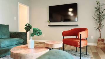 Un salon avec un canapé vert, un fauteuil rouge, une table basse et un téléviseur fixé au mur.