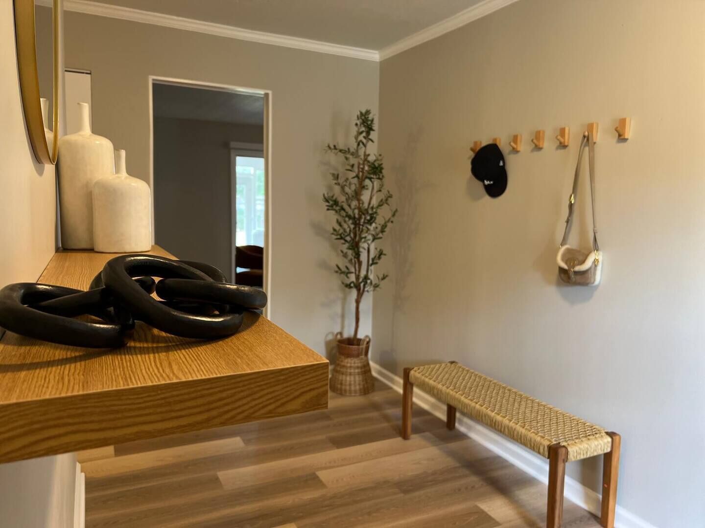 Une pièce moderne avec un banc en bois, une petite table sur laquelle sont posés des objets noirs enroulés, une plante en pot et un porte-manteau mural avec des chapeaux.