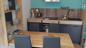Cocina compacta con una mesa y sillas de madera, estufa integrada y una pared de acento color verde azulado.