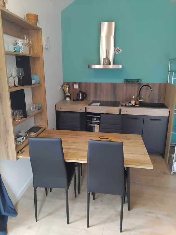 Cocina compacta con una mesa y sillas de madera, estufa integrada y una pared de acento color verde azulado.