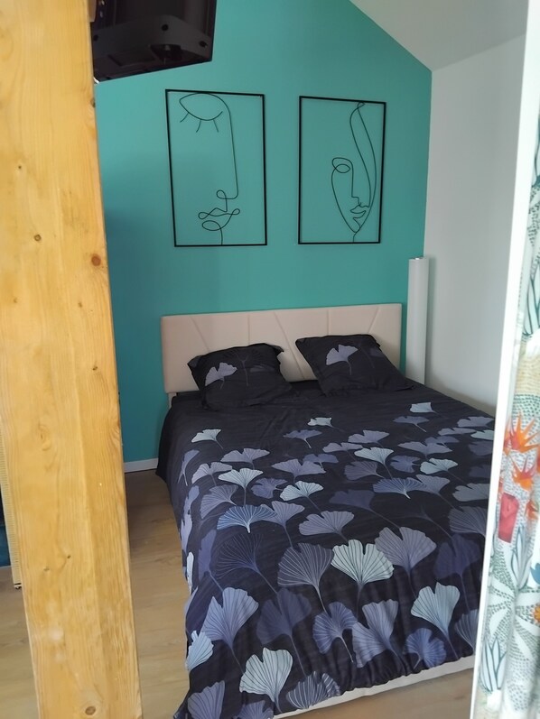 Un dormitorio con una cama, dos obras de arte en la pared y suelo de madera.