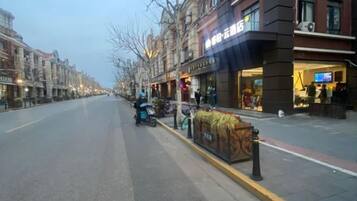 Una calle flanqueada por edificios, una scooter estacionada en la acera, y un local comercial con letreros iluminados.