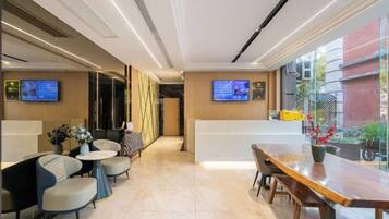A modern hotel lobby with a reception desk, seating area, and large windows.