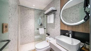 Een moderne badkamer met een douchecabine van glas, een wit toilet, een grote wasbak en een ronde spiegel.