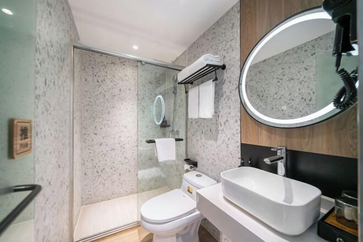 Een moderne badkamer met een douchecabine van glas, een wit toilet, een grote wasbak en een ronde spiegel.
