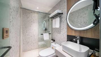 Un baño moderno con ducha de vidrio, inodoro blanco, lavabo grande y espejo redondo.