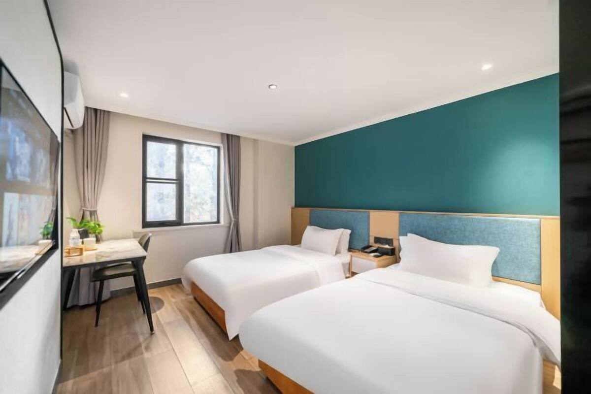 A hotel room with two beds, a desk, and a window.