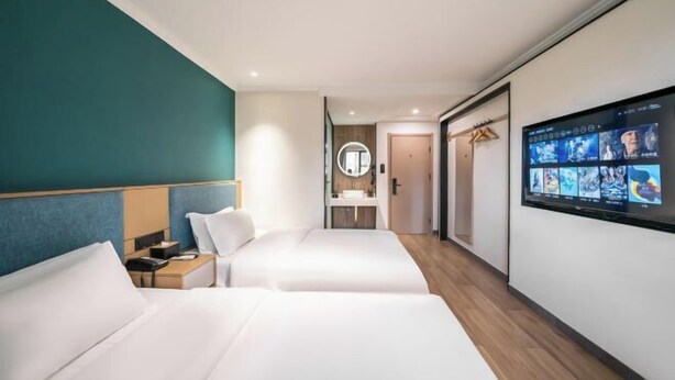 Een hotelkamer met twee bedden, een televisie, een spiegel en een badkamer op de achtergrond.