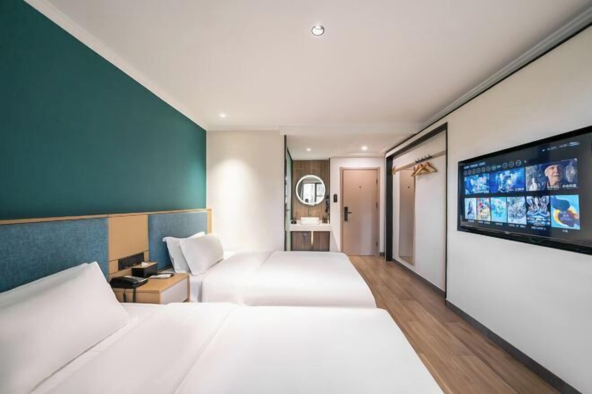 Een hotelkamer met twee bedden, een televisie, een spiegel en een badkamer op de achtergrond.