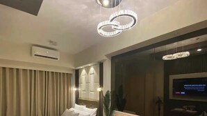 Un dormitorio moderno con cama, sofá, televisor y lámpara en el techo.