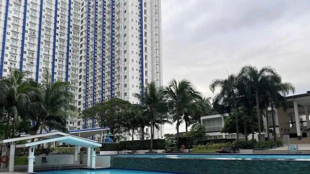 Una piscina con agua cristalina azul, rodeada de palmeras y un edificio residencial alto al fondo.