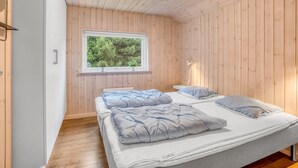 Une pièce aux murs en bois, une fenêtre donnant sur des arbres, deux lits avec des oreillers et un luminaire au plafond.
