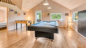 Une pièce au plancher de bois, équipée d’une table de billard, d’un baby-foot et d’un canapé.
