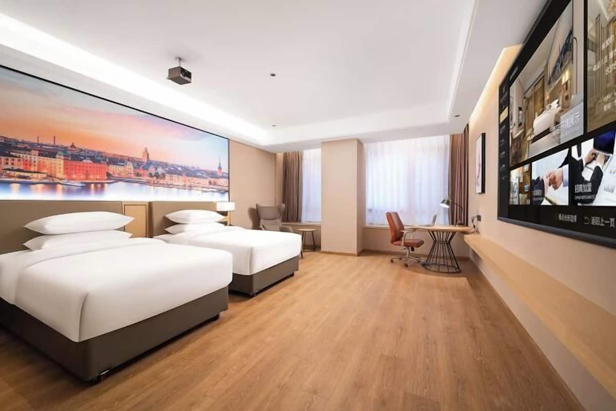 A hotel room with two beds, a desk, a chair, a TV, and a large window.