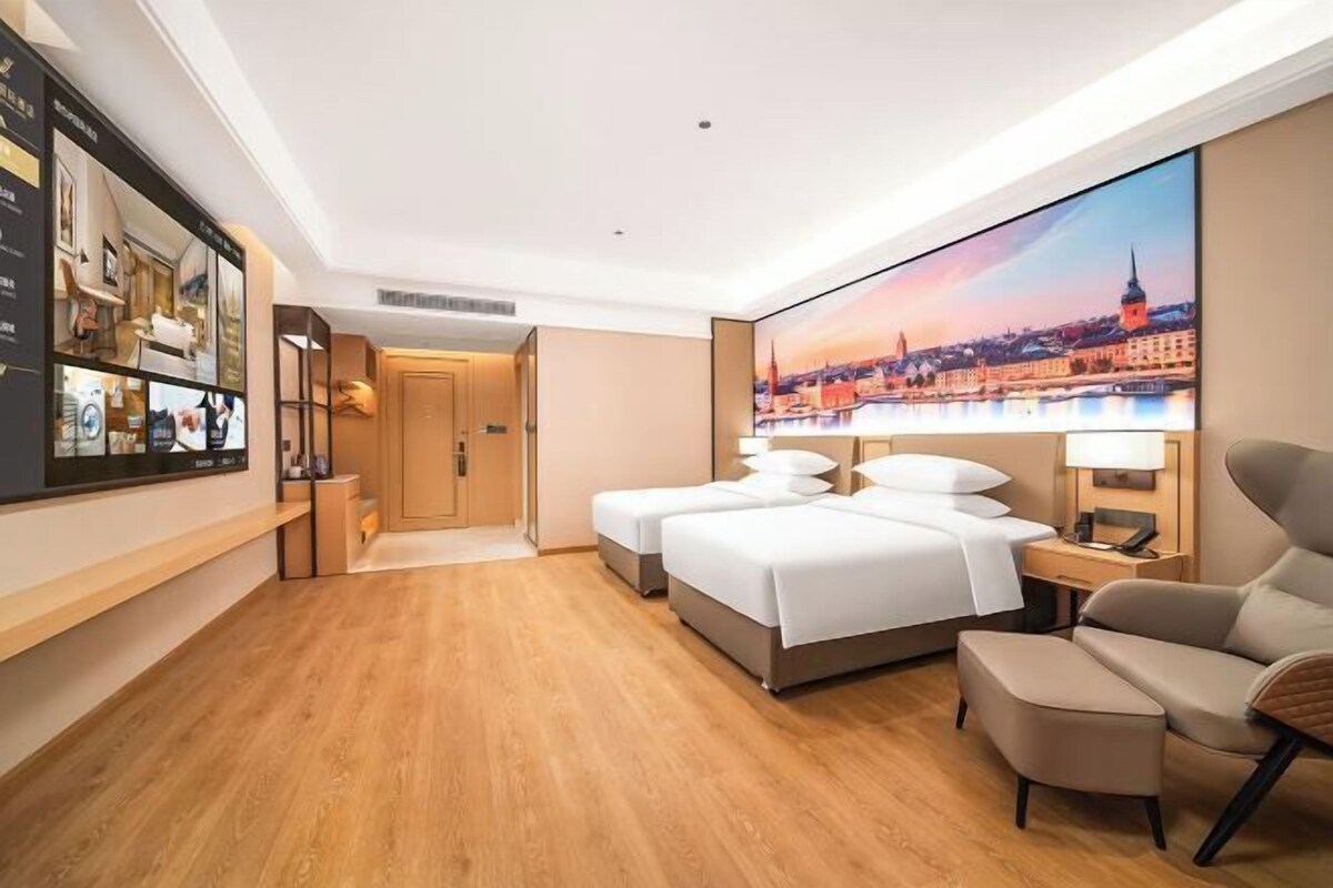 Quarto de hotel com uma cama grande, uma escrivaninha, uma cadeira e televisão presa à parede.