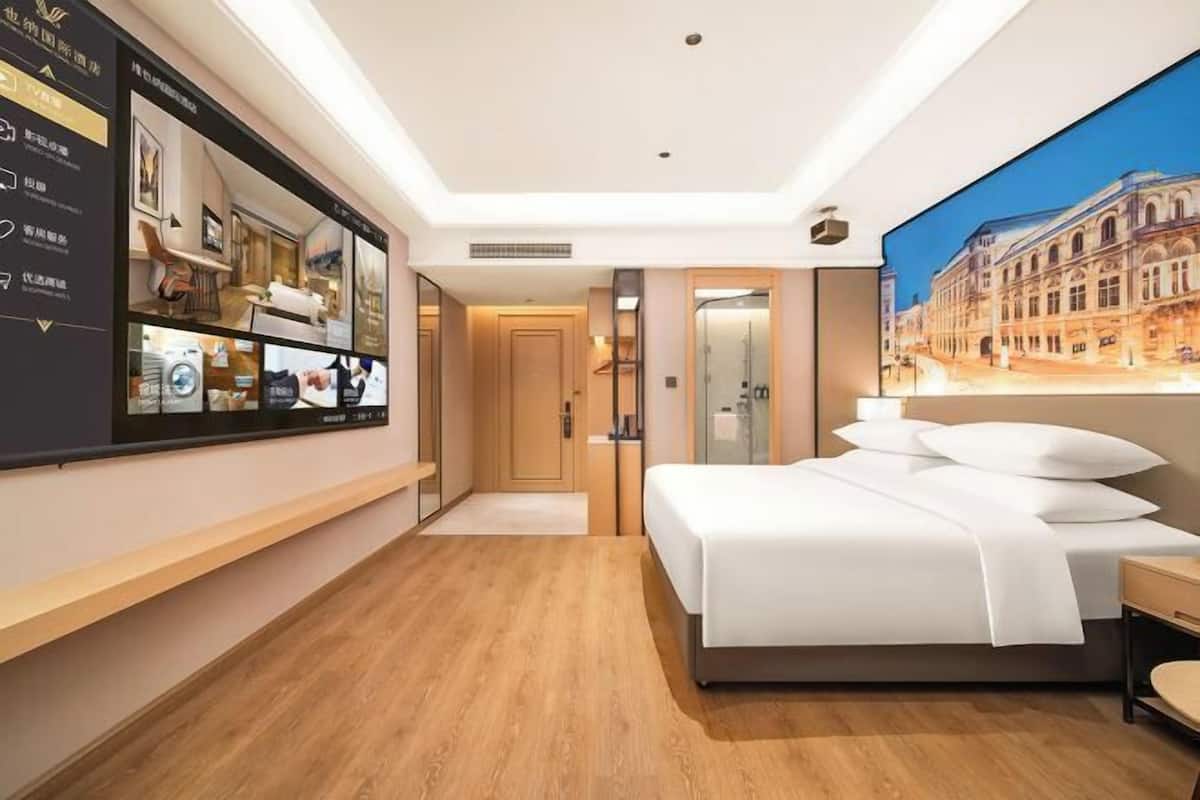 A modern hotel room with a large bed, a wall-mounted TV, and a cityscape mural.