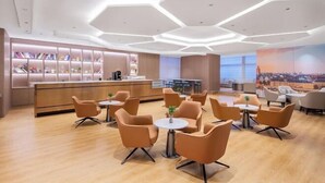 A modern hotel lobby with a central reception desk, multiple seating areas, and a cityscape mural on the wall. - Vienna International Hotel(ShenzhenLuohu Shuibei Jewelry City Branch) (Shenzhen)