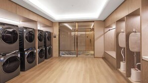 A modern laundry facility with multiple washing machines and dryers, wooden paneling, and a glass elevator. - Vienna International Hotel(ShenzhenLuohu Shuibei Jewelry City Branch) (Shenzhen)