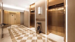 A modern hotel lobby with a checkered floor, a reception desk, and two elevators. - Vienna International Hotel(ShenzhenLuohu Shuibei Jewelry City Branch) (Shenzhen)