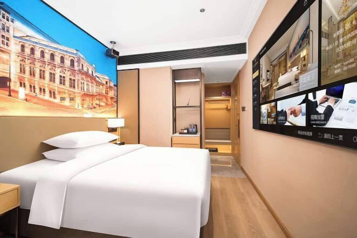 A hotel room with a bed, a nightstand, a wall-mounted TV, and a large window.