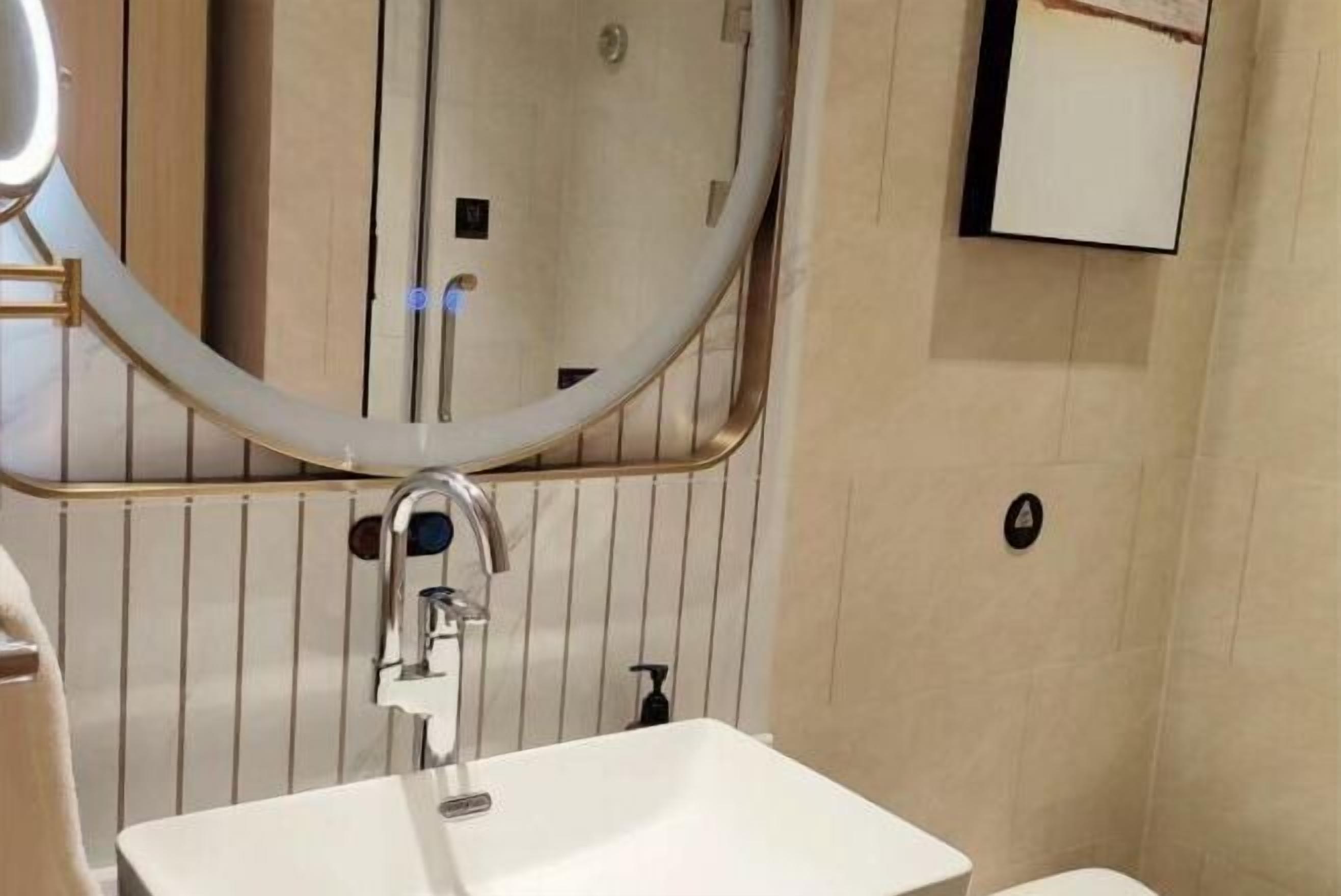 A bathroom with a white sink, a round mirror, and a toilet.