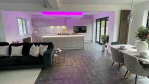 A modern kitchen with white cabinets, a central island, and purple under-cabinet lighting. - Branksome 4-house Sleeps 8 With Hot Tub & Parking (Worcester)