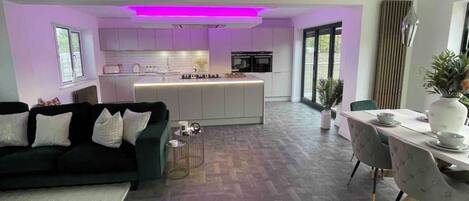 A modern kitchen with white cabinets, a central island, and purple under-cabinet lighting.
