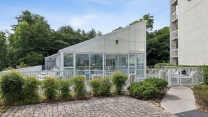A modern building with a glass facade, surrounded by a white fence and greenery.